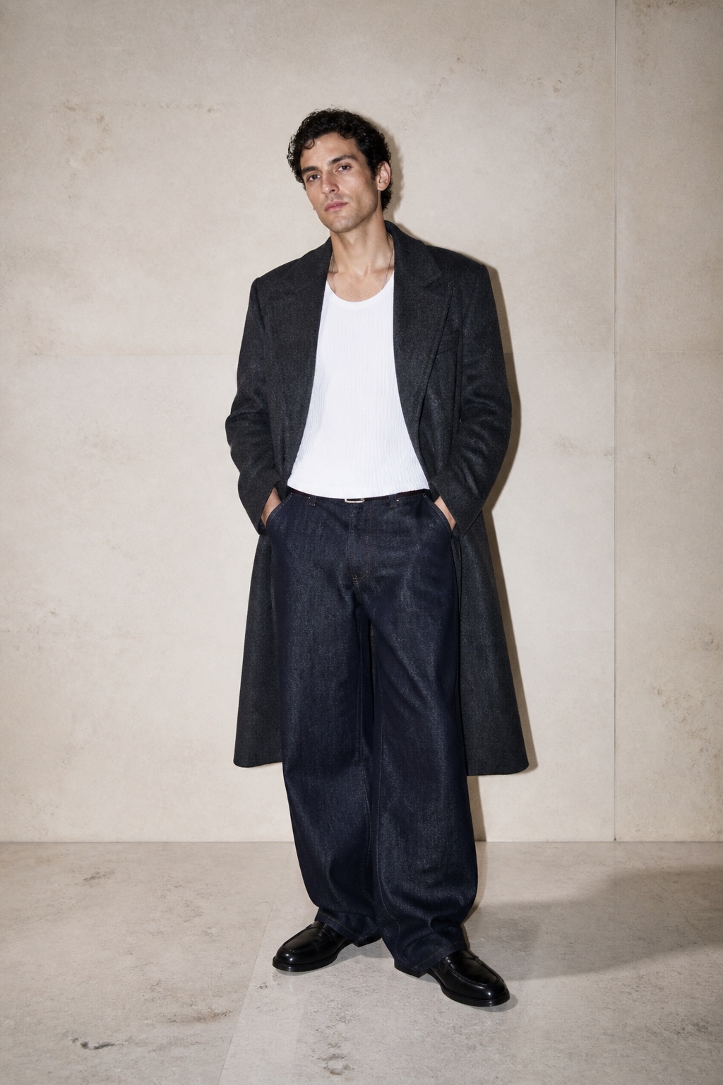 Man wearing a charcoal overcoat, white ribbed shirt, wide dark jeans, and black loafers